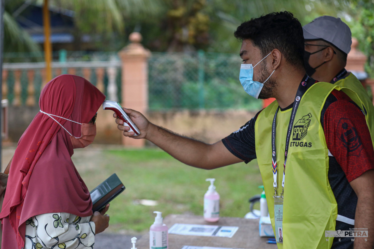 Seorang petugas SPR mengimbas suhu pengundi di SK Durian Daun. - Gambar Azim Ab Rahman