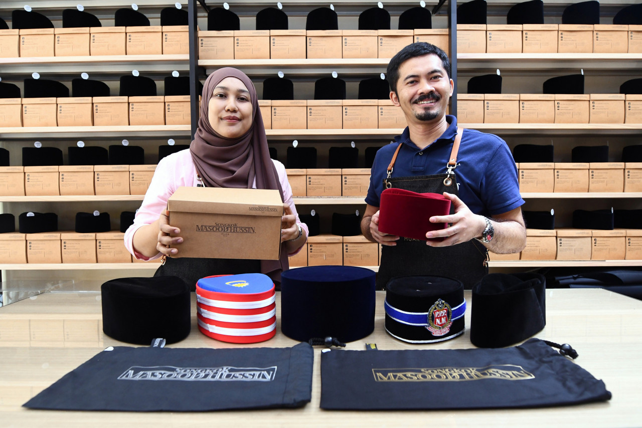 Nurdalila bersama suaminya Zahedy Zakariah, 43, menunjukkan songkok yang dihasilkannya setelah mewarisi bakat membuatnya daripada datuknya, Masood Hussin. Gambar: Kamarul Halim M Kamal, Bernama