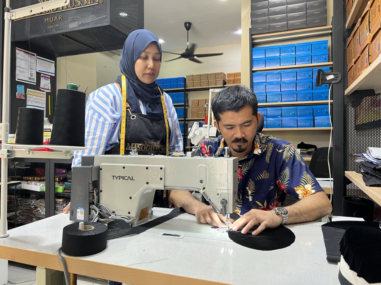 Pemilik perniagaan songkok Masood Hussin atau lebih dikenali ‘Songkok Muar’, Nurdalila (kiri) bersama suaminya, Zahedy menunjukkan cara menjahit songkok lipat yang kini menjadi kegilaan anak muda kerana ianya mudah dibawa. - Gambar Bernama
