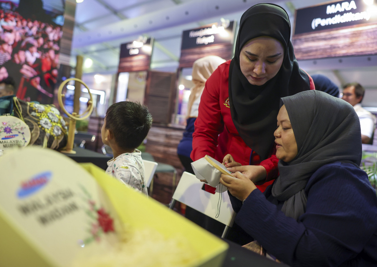 Tenaga Pengajar Pemaju Masyarakat Kemahiran Jahitan dari Kemas Wilayah Persekutuan Sharifah Raudhah Sy Dahalan (kiri) memberi peluang kepada orang ramai untuk mencuba teknik sulaman tangan di reruai Kementerian Desa dan Wilayah sempena Program Setahun Bersama Kerajaan MADANI di Stadium Nasional Bukit Jalil semalam. – gambar BERNAMA