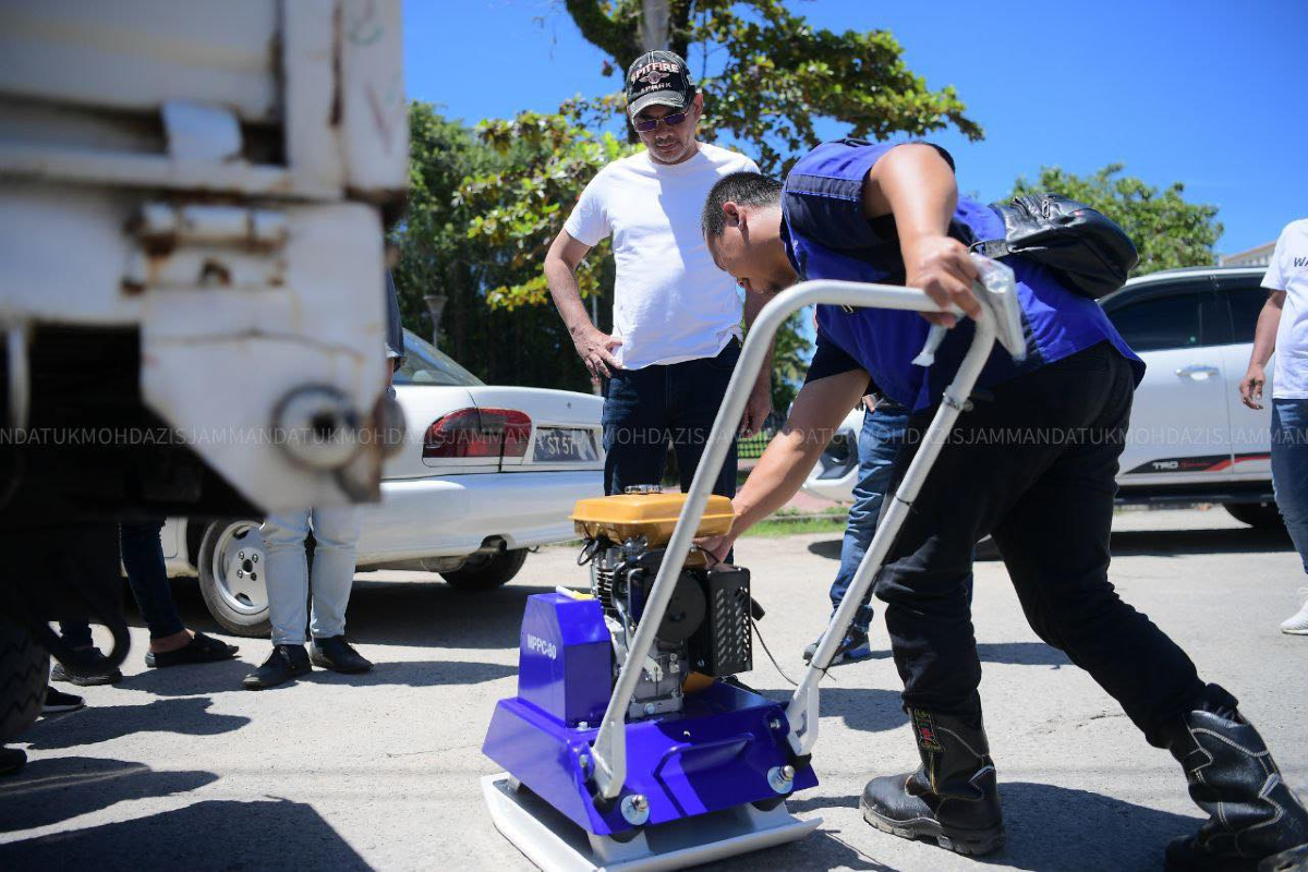 Azis (kiri) membeli sendiri mesin kompak untuk membaiki jalan rosak di kawasannya.