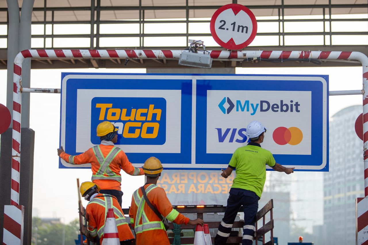 Pekerja lebuh raya memasang papan tanda laluan yang boleh menggunakan kaedah pembayaran kad bank dan kad kredit selain kad prabayar Touch N Go. - gambar Facebook