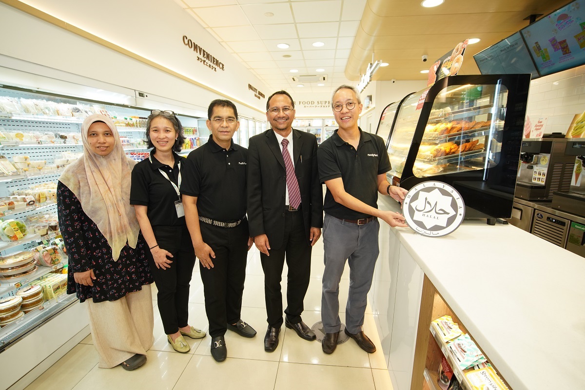 Chia Lik Khai menampal logo halal pada penyejuk makanan ringan panas, disaksikan Razi Hassan. - Gambar FamilyMart Malaysia