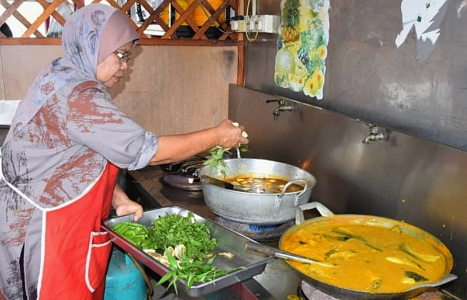 Zaharah sedang memasak gulai biji getah.