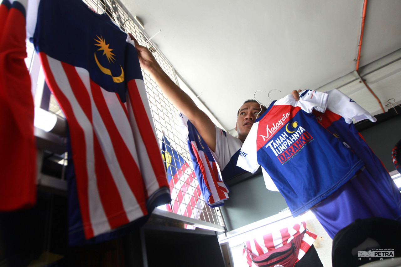 Khairulnizam Rahim menyusun baju bertemakan Jalur Gemilang di kedainya Stesen LRT Taman Melati. gambar Azlan Hadi Abu Bakar