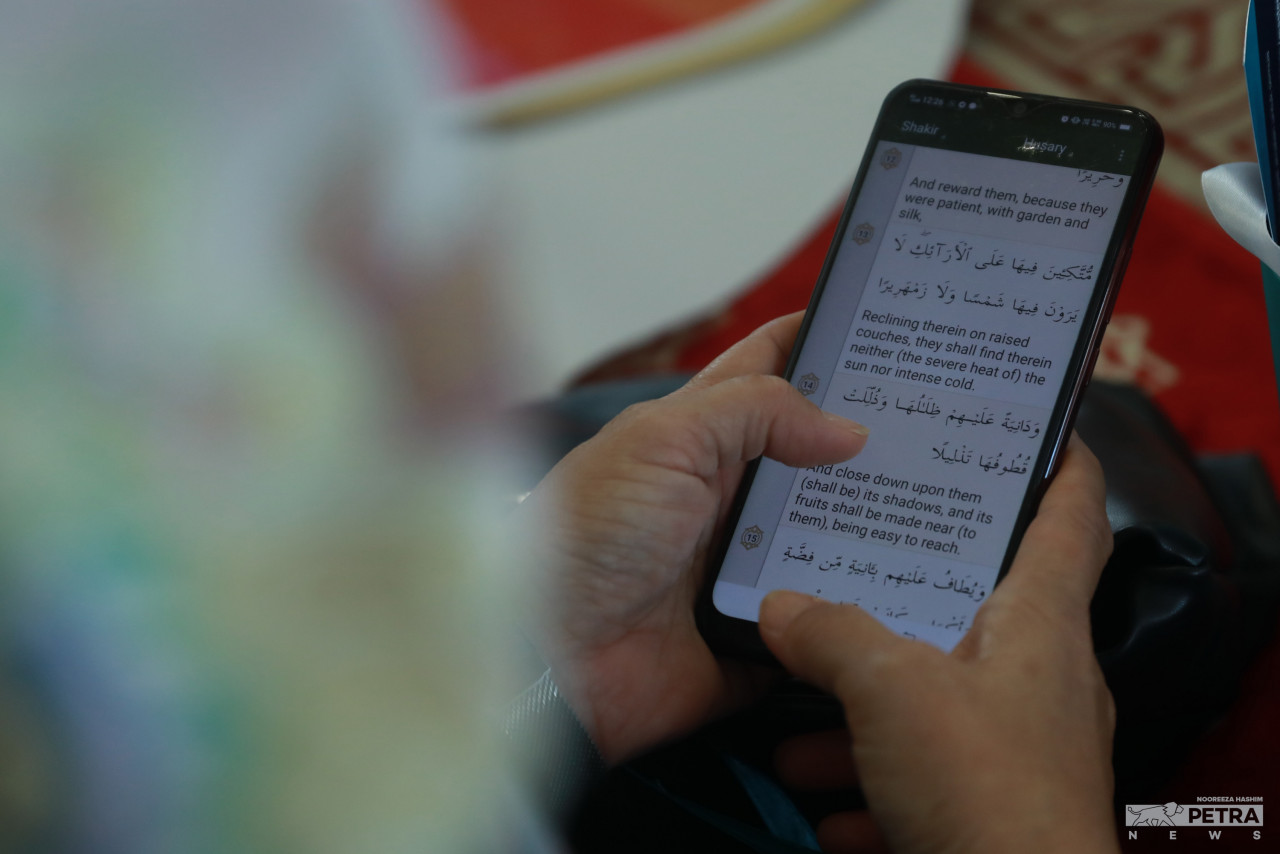 Salah seorang peserta Malaysia #QuranHour membaca ayat Al-Quran menggunakan telefon bimbitnya.