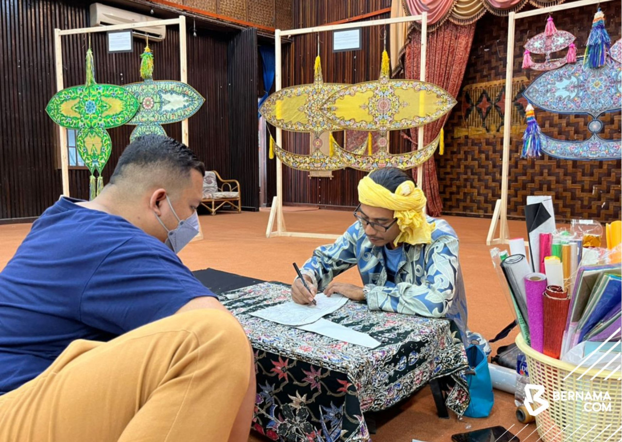 Muhd Azeimi (kanan) tekun melukis pada wau rekaannya. - Gambar Bernama