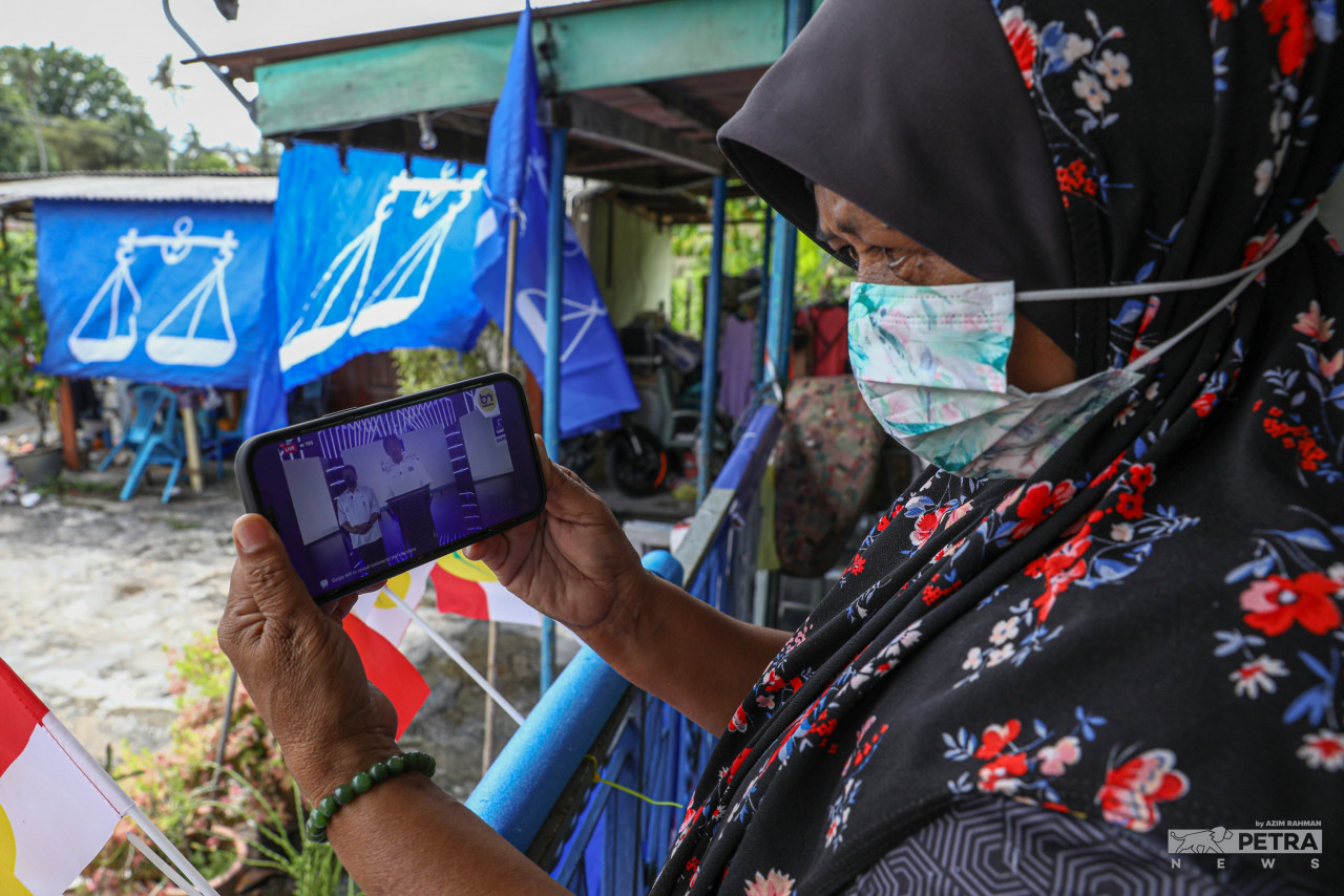 Seorang warga emas mendengar ucapan yang disampaikan calon yang bertanding pada PRN Melaka menerusi media sosial.