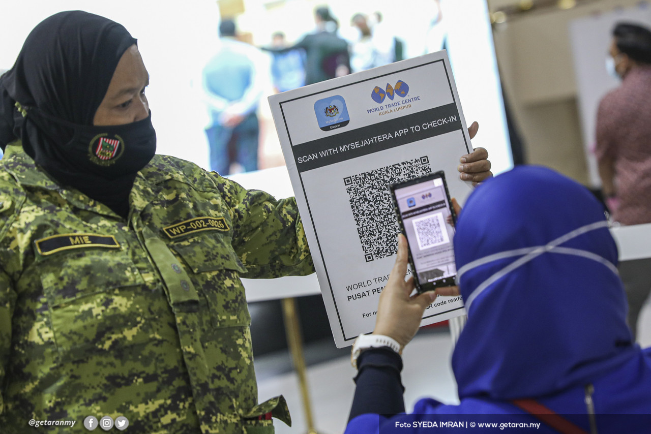 Seorang pegawai RELA membantu seorang pengunjung untuk mengimbas kod QR MySejahtera sebelum dibenarkan masuk ke PPV WTCKL. - Gambar oleh Syeda Imran