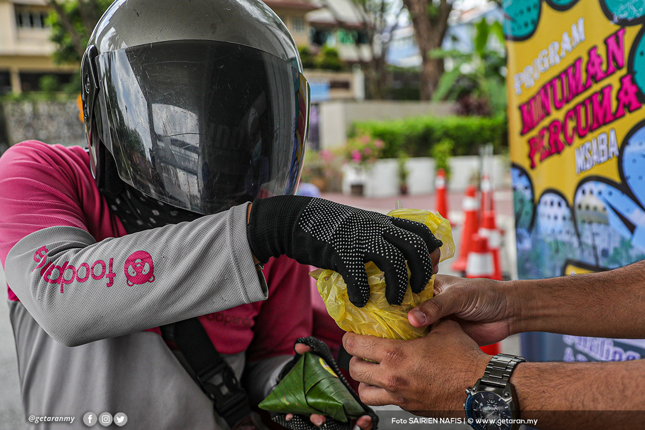 Seorang penunggang e-hailing menerima bungkusan makanan daripada seorang jemaah masjid. 