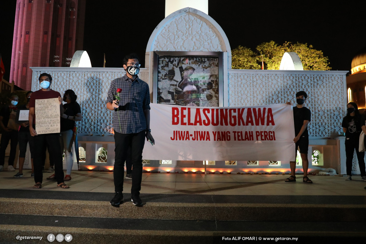 Seorang penunjuk perasaan berdiri di depan kain rentang yang tertulis ‘belasungkawa jiwa-jiwa yang telah pergi’.