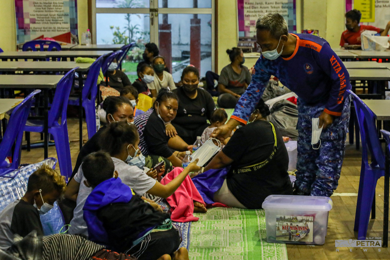 Seorang petugas di PPS Pulau Indah menyerahkan pelitup muka kepada mangsa banjir yang dipindahkan ke situ.