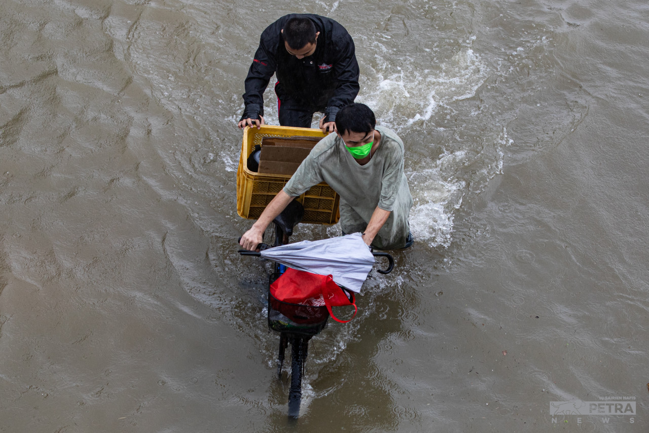 Dua orang lelaki meredah air banjir di Taman Seri Lembayung, Shah Alam. - Gambar oleh Sairien Nafis