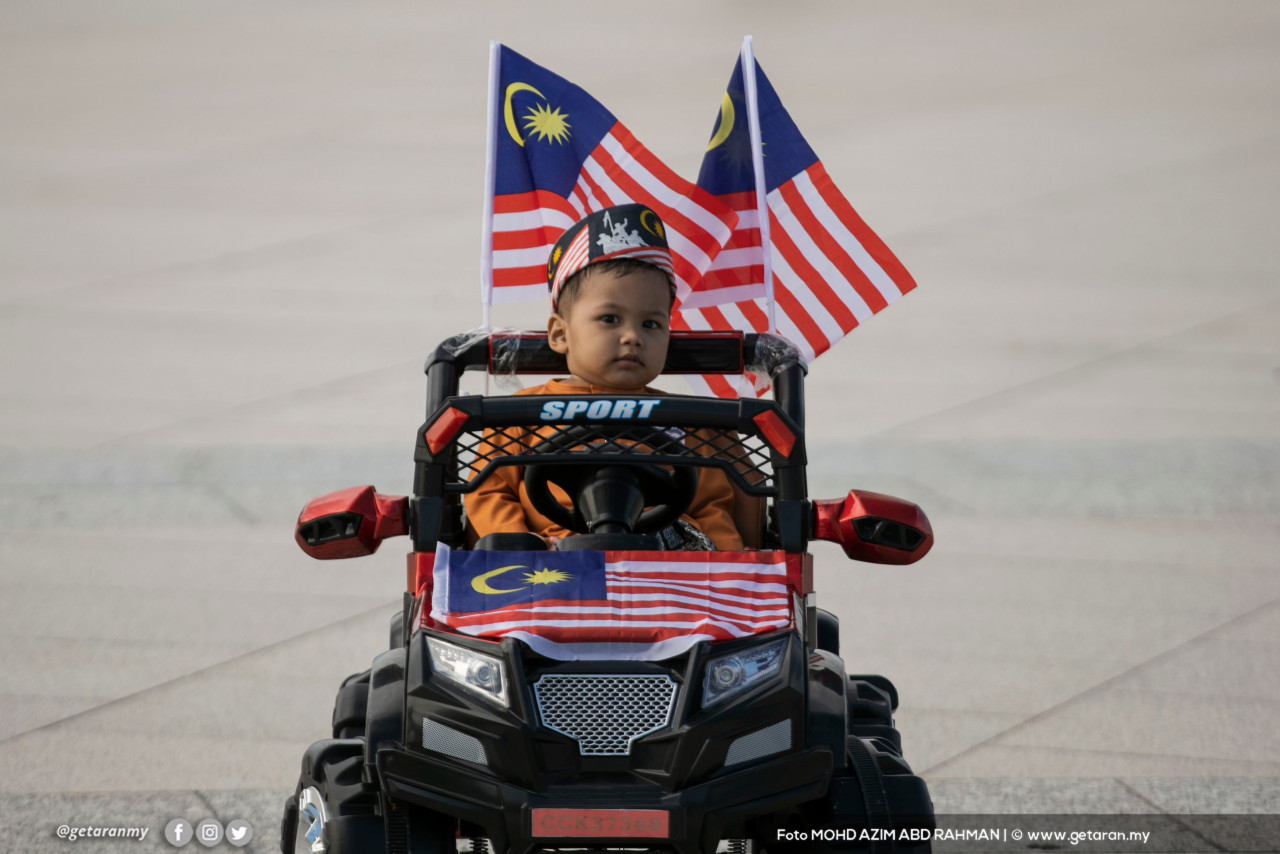 Seorang kanak-kanak menaiki kereta mainan yang dihiasi dengan Jalur Gemilang. - Gambar oleh Azim Rahman