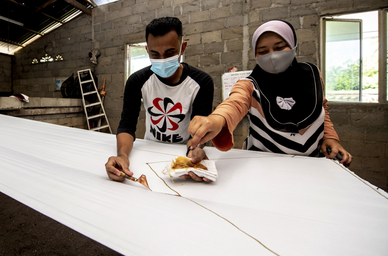 Yuslinawati (kanan) bersama sepupunya Wan Hafizul mencanting lilin di atas kain putih untuk membuat bendera Palestin ketika ditemu di rumahnya di Kampung Baru Salor. - Gambar Bernama