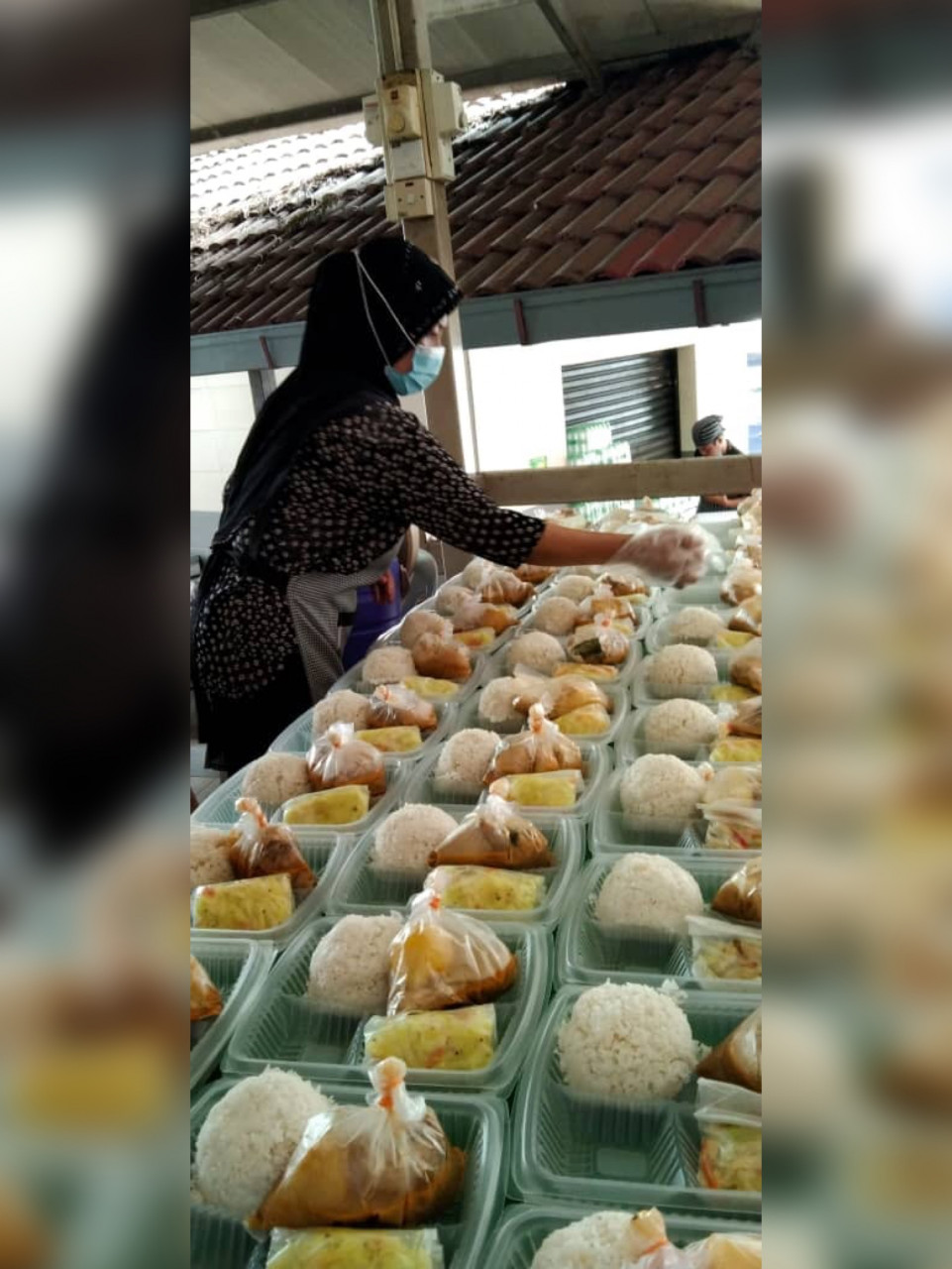Seorang sukarelawan meyiapkan pek makanan untuk diedarkan. - Gambar dari Facebook