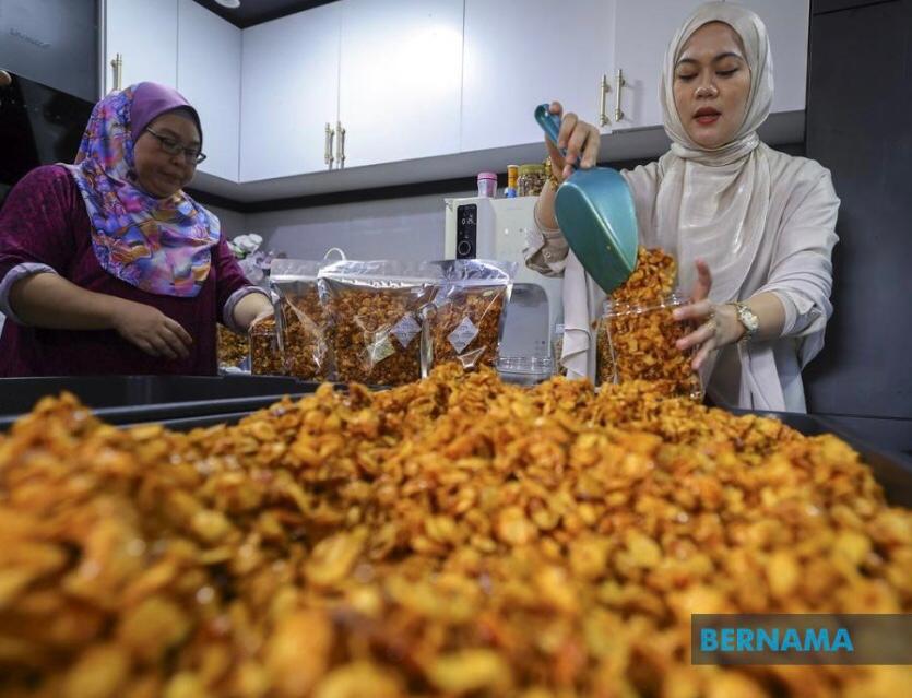 Nurul Arfiqah Ali (kanan) memasukkan kudapan pedas berasaskan emping jagung ke dalam balang. 