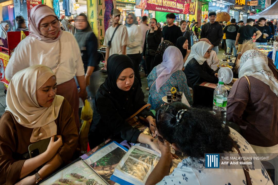 Peniaga menghiasi tangan pelanggan dengan inai.