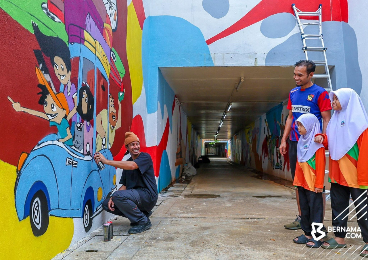 Muhammad Fakhrul Akmal Shamsurrijal (kiri) melayani orang ramai yang menyapanya semasa menyiapkan lakaran grafiti untuk Perbadanan Putrajaya di kawasan laluan pejalan kaki di Presint 8. gambar BERNAMA